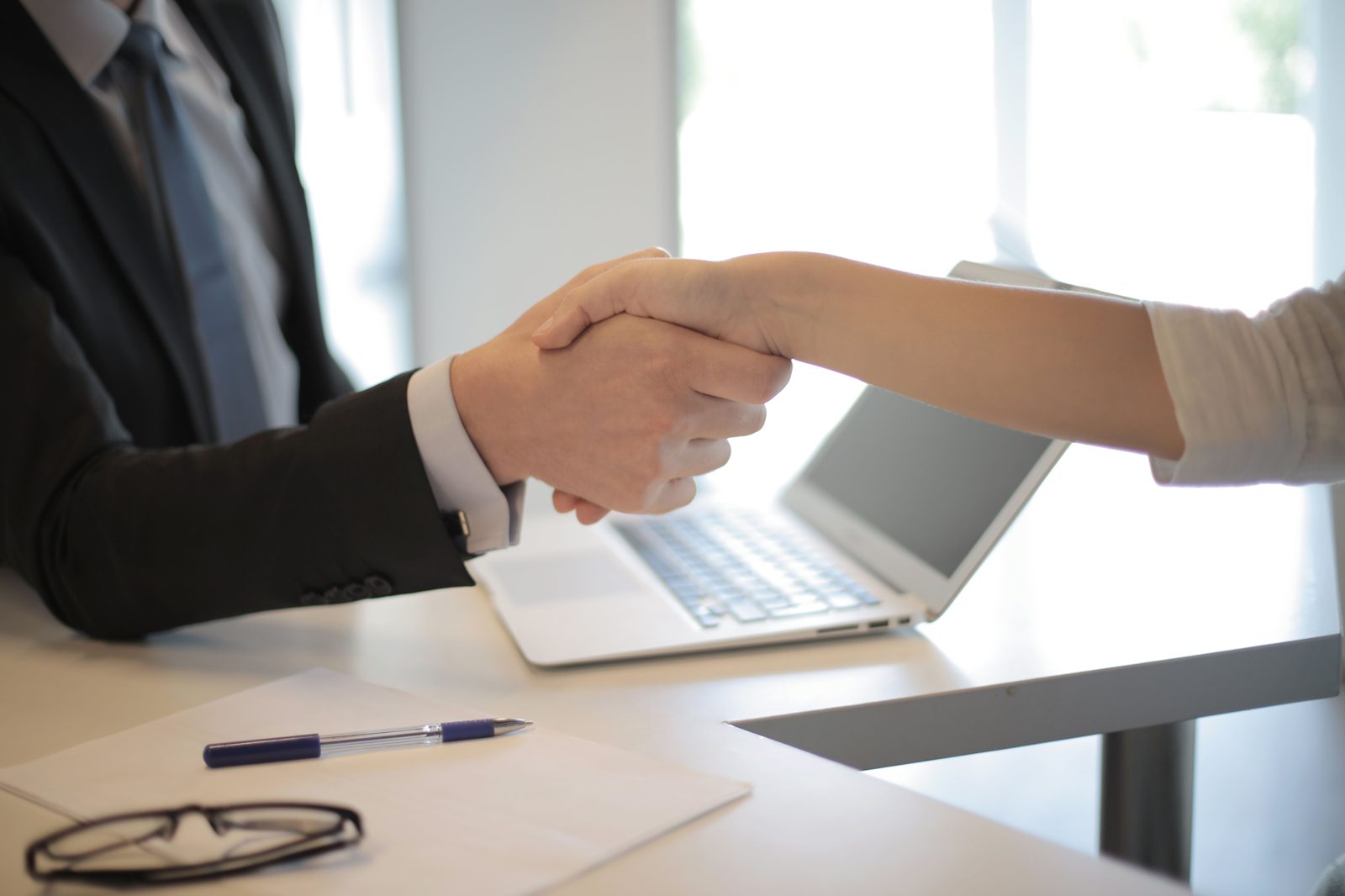 Two people shaking hands over a laptop at a desk